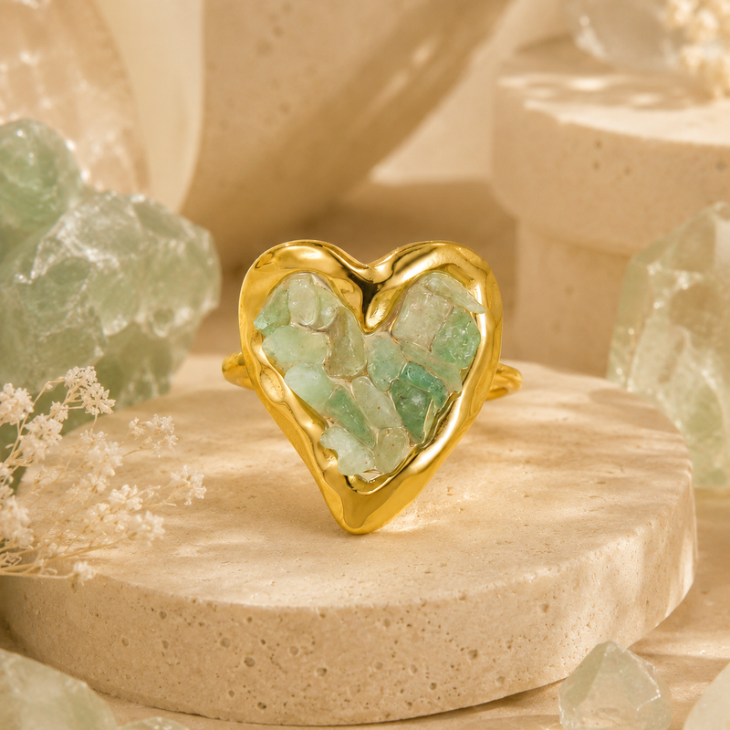 Orphaya gold heart ring featuring natural green aventurine crystal chips on a warm beige stone background.