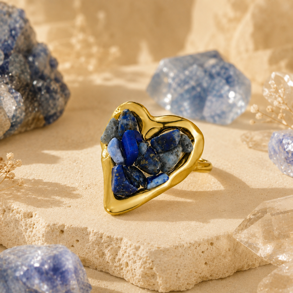 Orphaya gold heart ring filled with deep blue lapis lazuli crystal chips, styled on a soft beige stone surface.