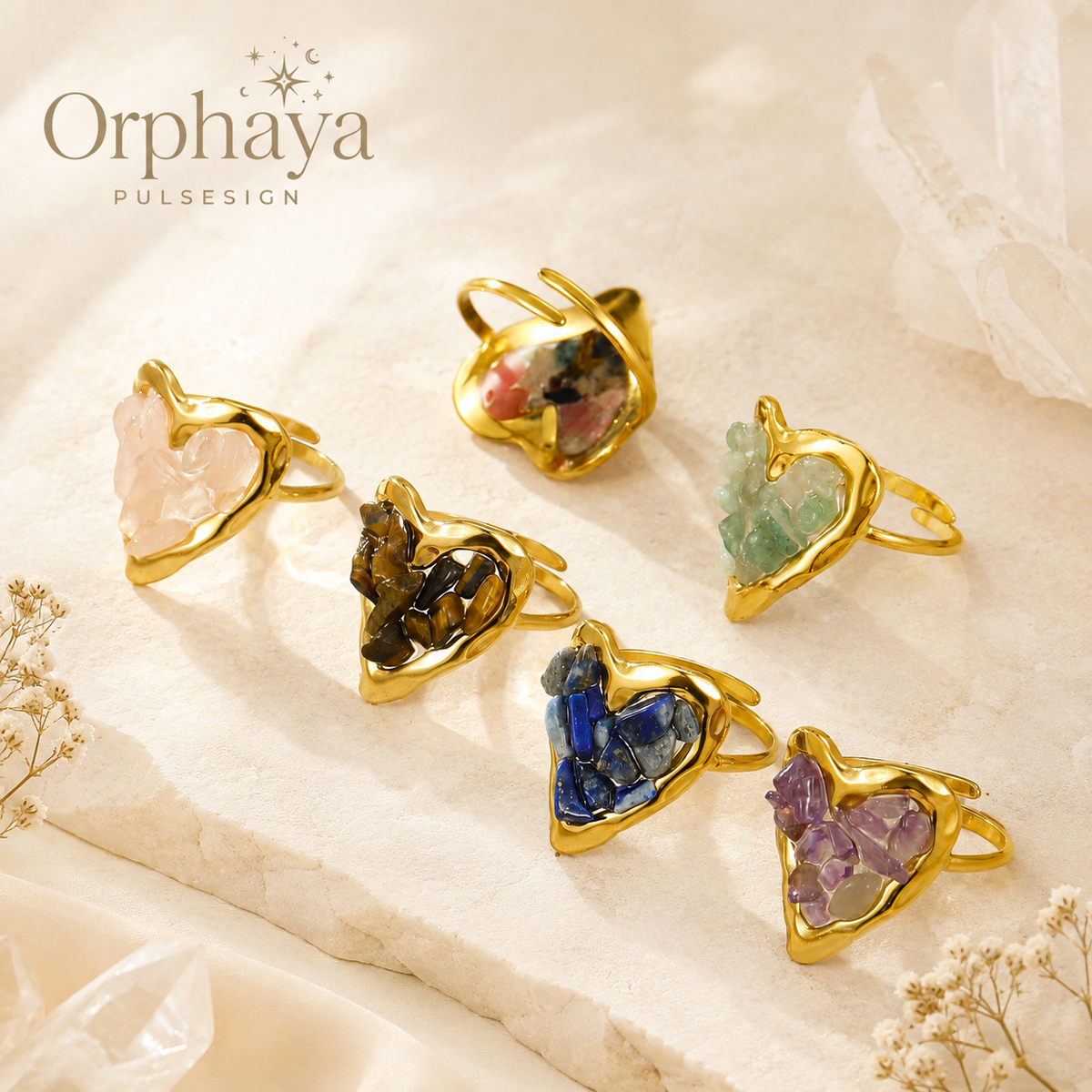 Orphaya heart crystal ring collection featuring six gold-tone adjustable rings with natural crystal chip inlays, displayed on a soft beige stone surface with clear crystal accents in an elegant spiritual jewelry style.