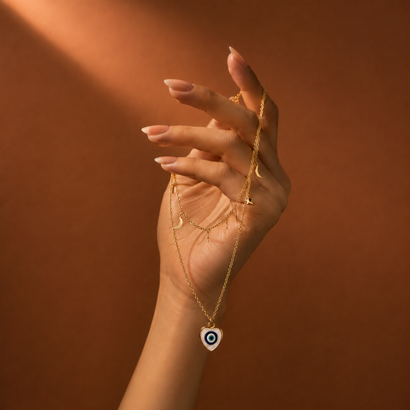 Close-up of gold NFC evil eye necklace held in hand with warm brown background